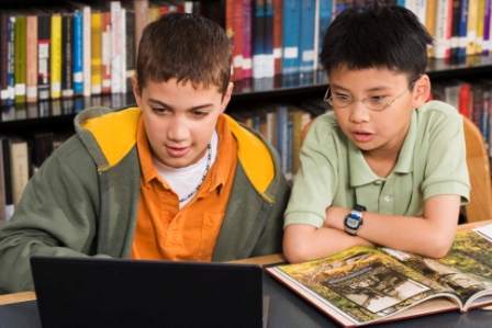 Boys using laptop in library